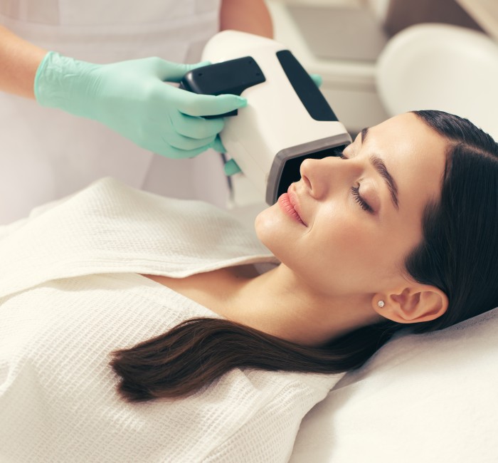 calm young woman smiling with closed eyes while beautician rubber gloves holding skin analysis camera near her face 1